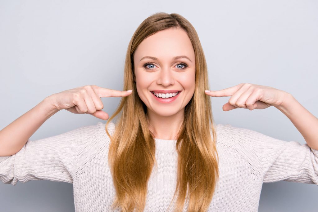 young woman smiling and pointing at her veneers in Simpsonville, SC