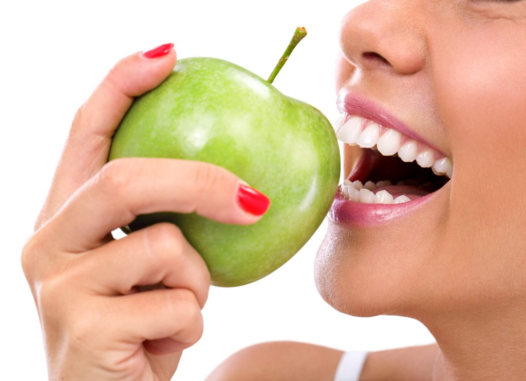 woman eats apple to avoid dental issues and cosmetic dentist in Greenville SC