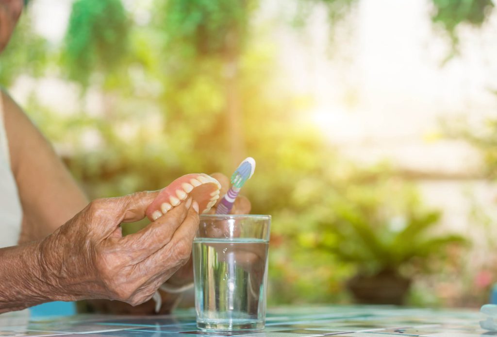 a senior brushing his dentures as advised by a Dentist in Greenville SC